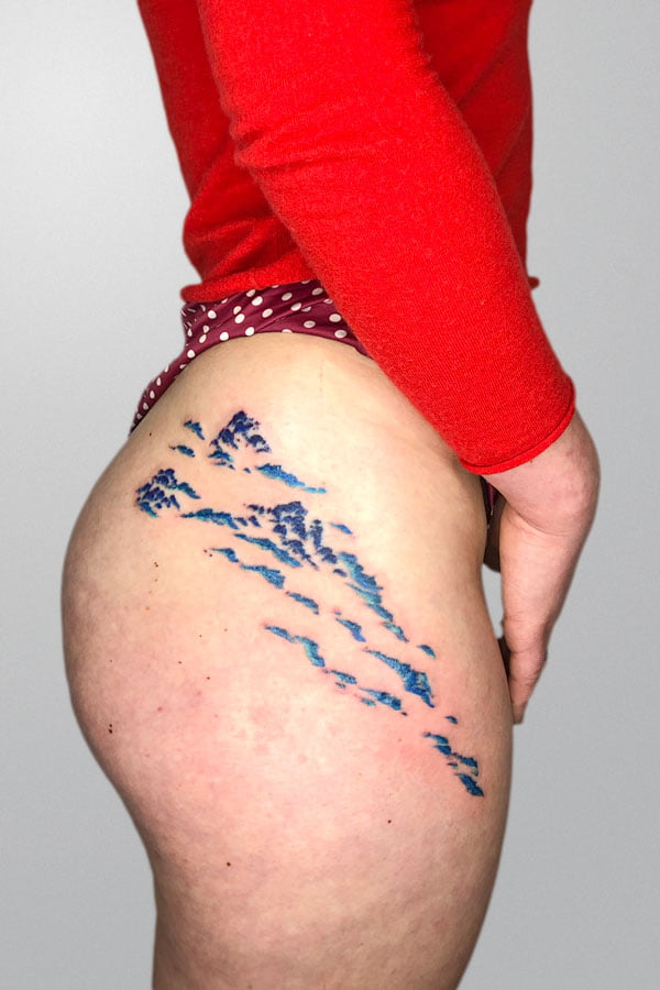 hip tattooed with blue rocks and sea